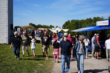 Besucher schlendern über ein Festgelände mit Ständen und Aktivitäten