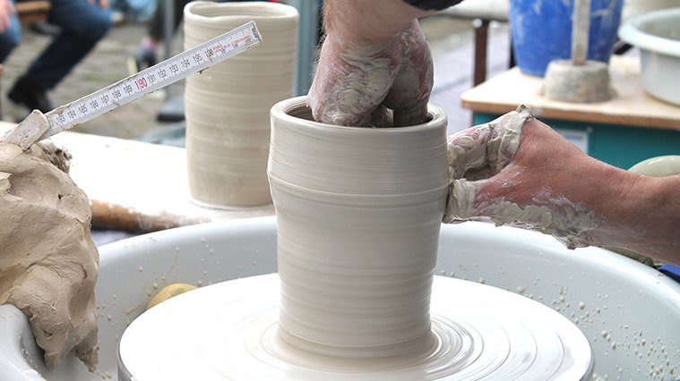 Eine Hand formt einen Becher aus Ton auf einer Töpferscheibe