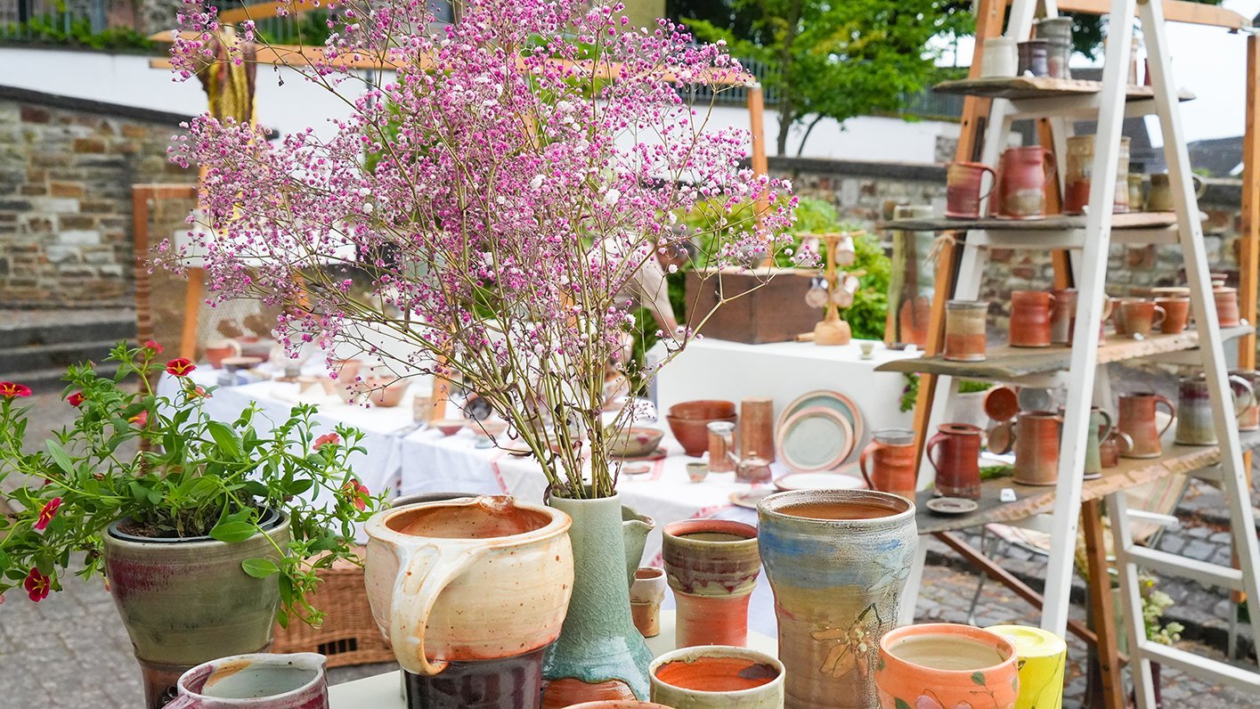 Verschiedene Töpferwaren und Blumen auf einem Marktstand im Freien